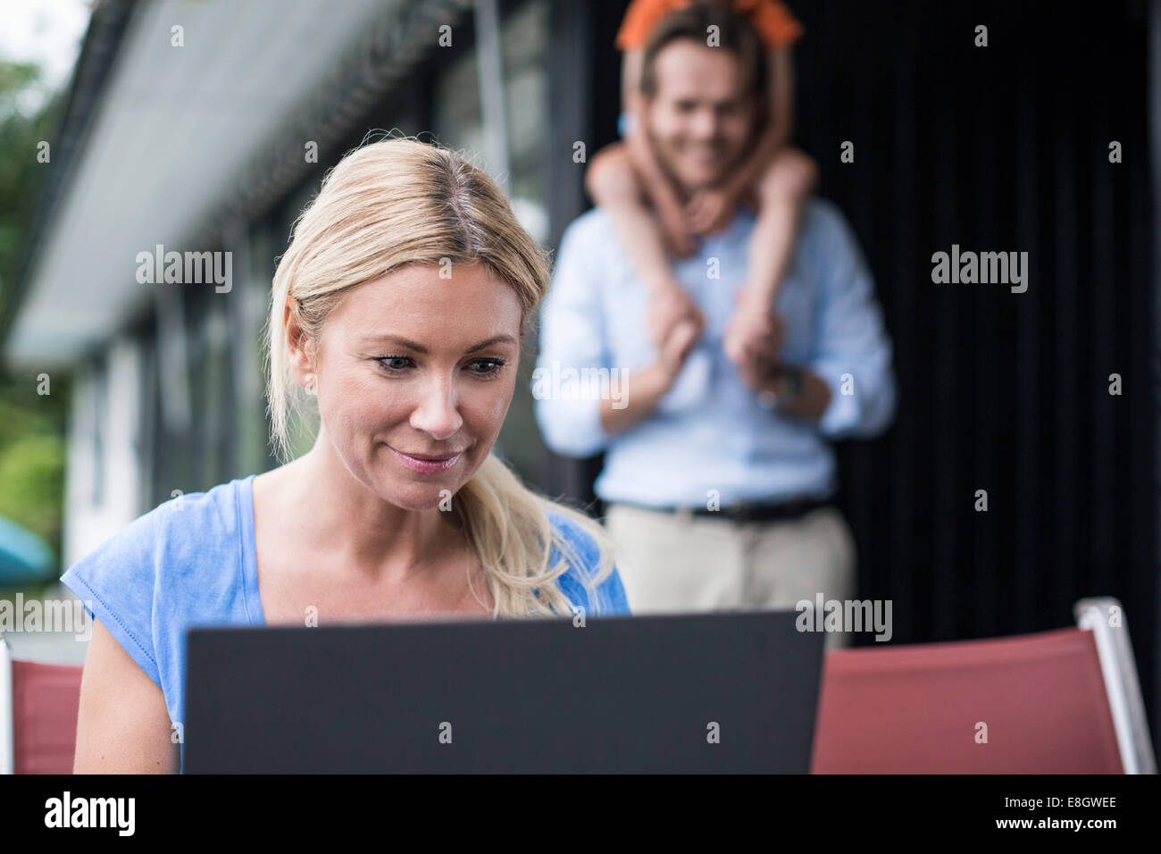 Frau mit Laptop am Hof mit Familie im Hintergrund Stockfoto