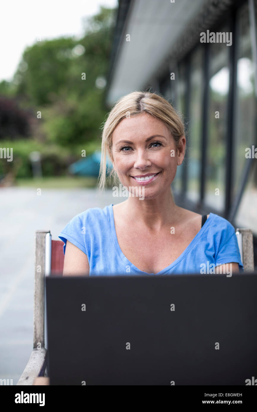 Porträt der glückliche Frau mit Laptop im Garten sitzen Stockfoto