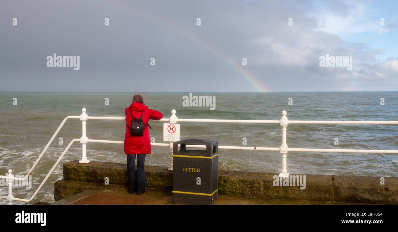 Bridlington, England, 10. August: Dame in rot Blick auf einem Regenbogen, während stürmisches Wetter die Küstenlinie, 10. August verprügelt: 2014 Stockfoto
