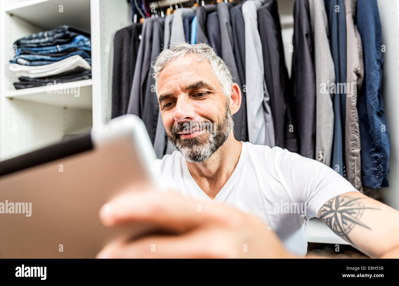 Mann mit seinem digitalen Tablet sitzen auf dem Boden seiner begehbaren Kleiderschrank Stockfoto