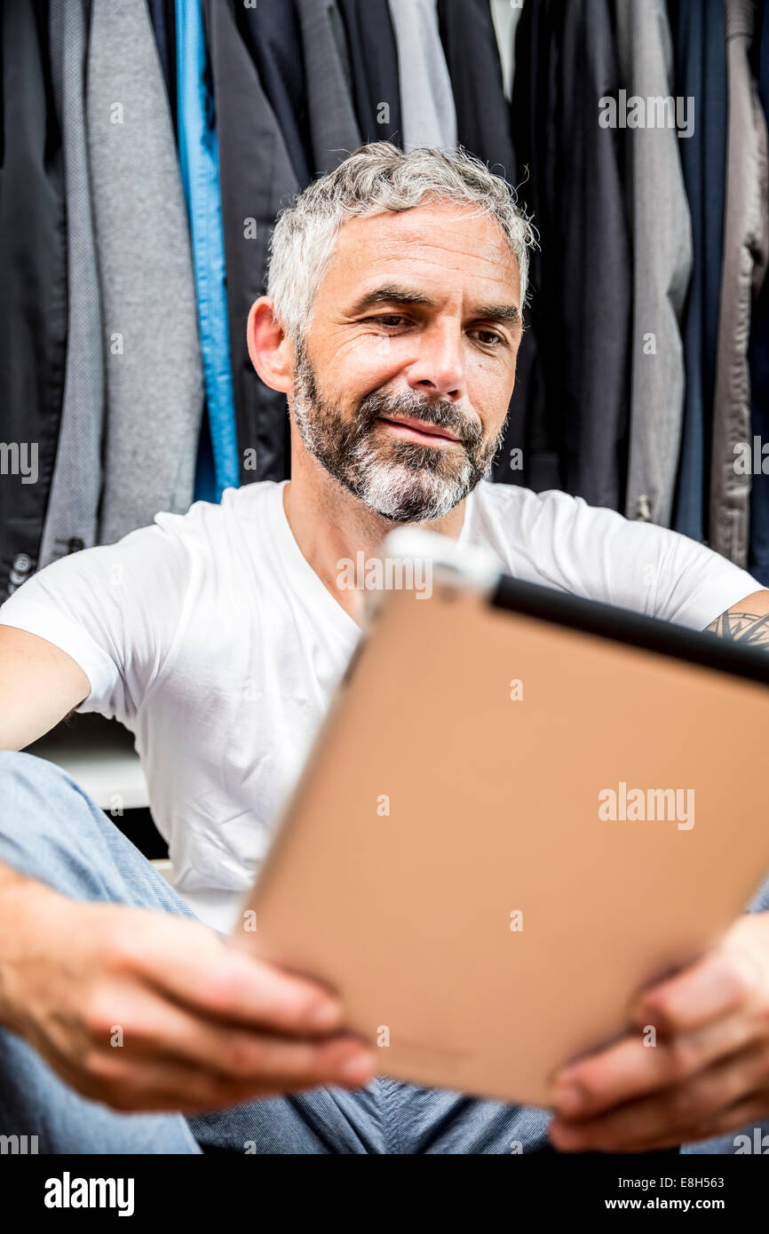 Mann mit seinem digitalen Tablet sitzen auf dem Boden seiner begehbaren Kleiderschrank Stockfoto