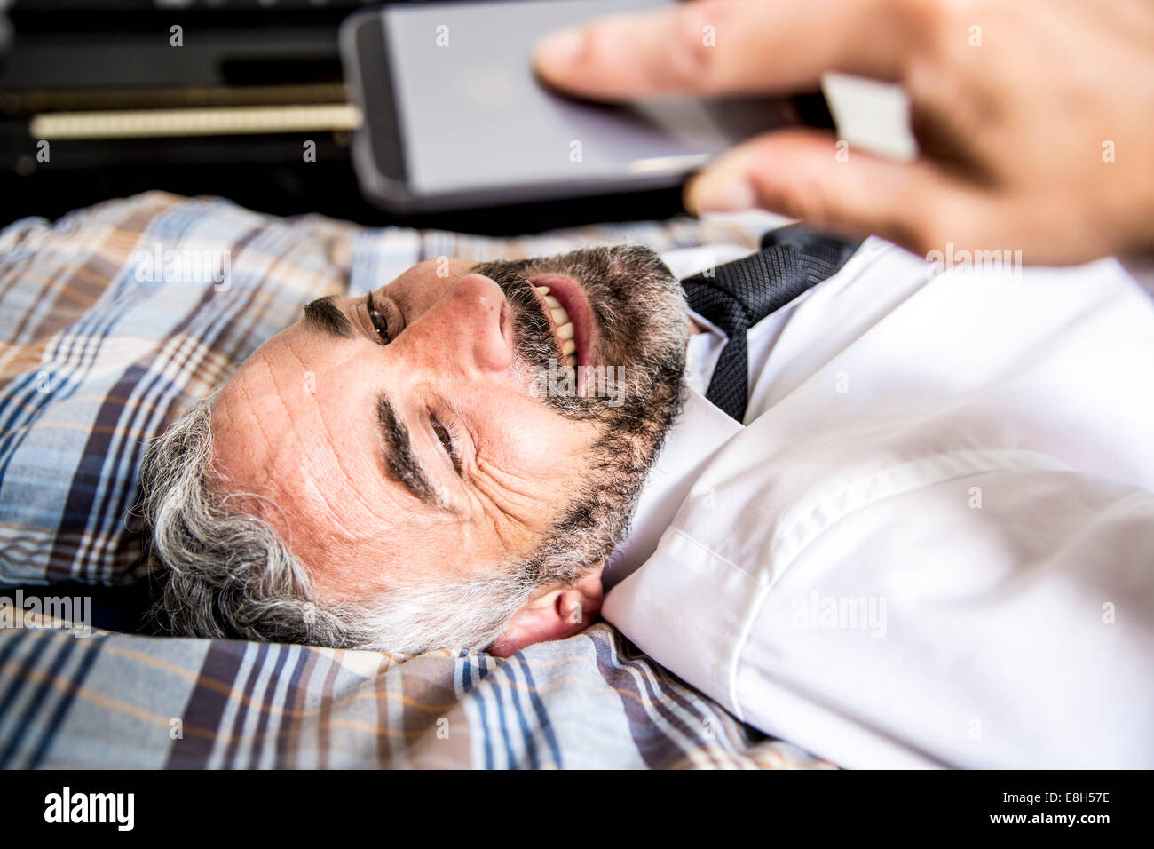 Porträt von lächelnden Geschäftsmann liegt auf seinem Bett, Blick auf seinem smartphone Stockfoto