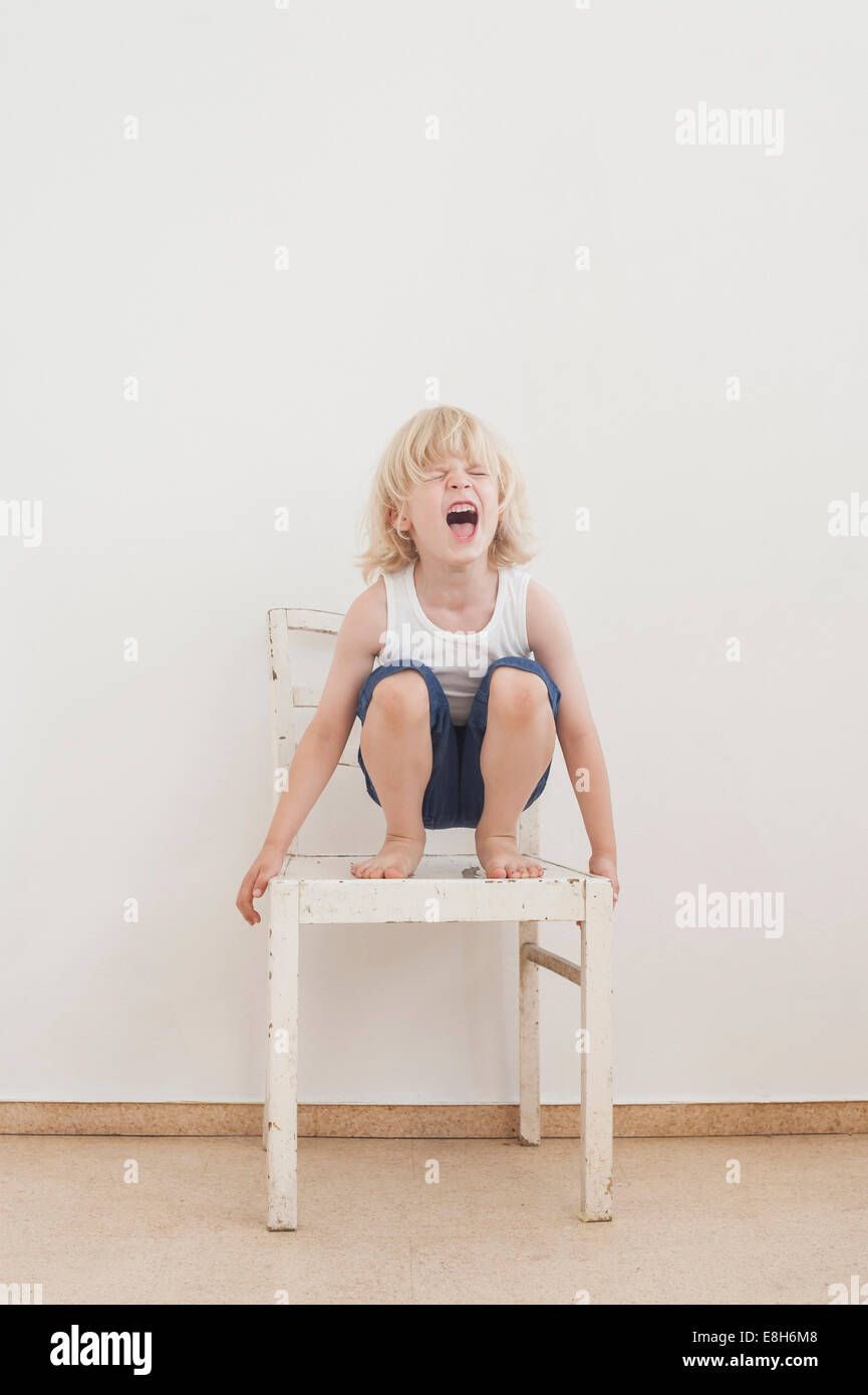 Porträt von schreien kleine Junge Crounching auf einem Stuhl Stockfoto