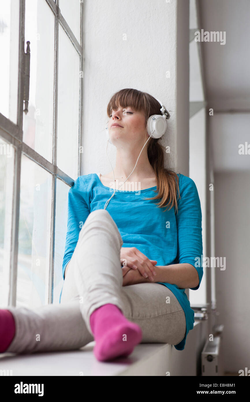 Portrait von junge Frau sitzt auf der Fensterbank in einem Büro Musik hören mit Kopfhörern Stockfoto