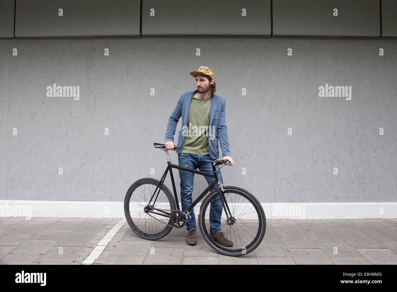 Deutschland, Bayern, München, junger Mann mit Basecap stehen vor einer Wand mit seinem Renn-Zyklus Stockfoto