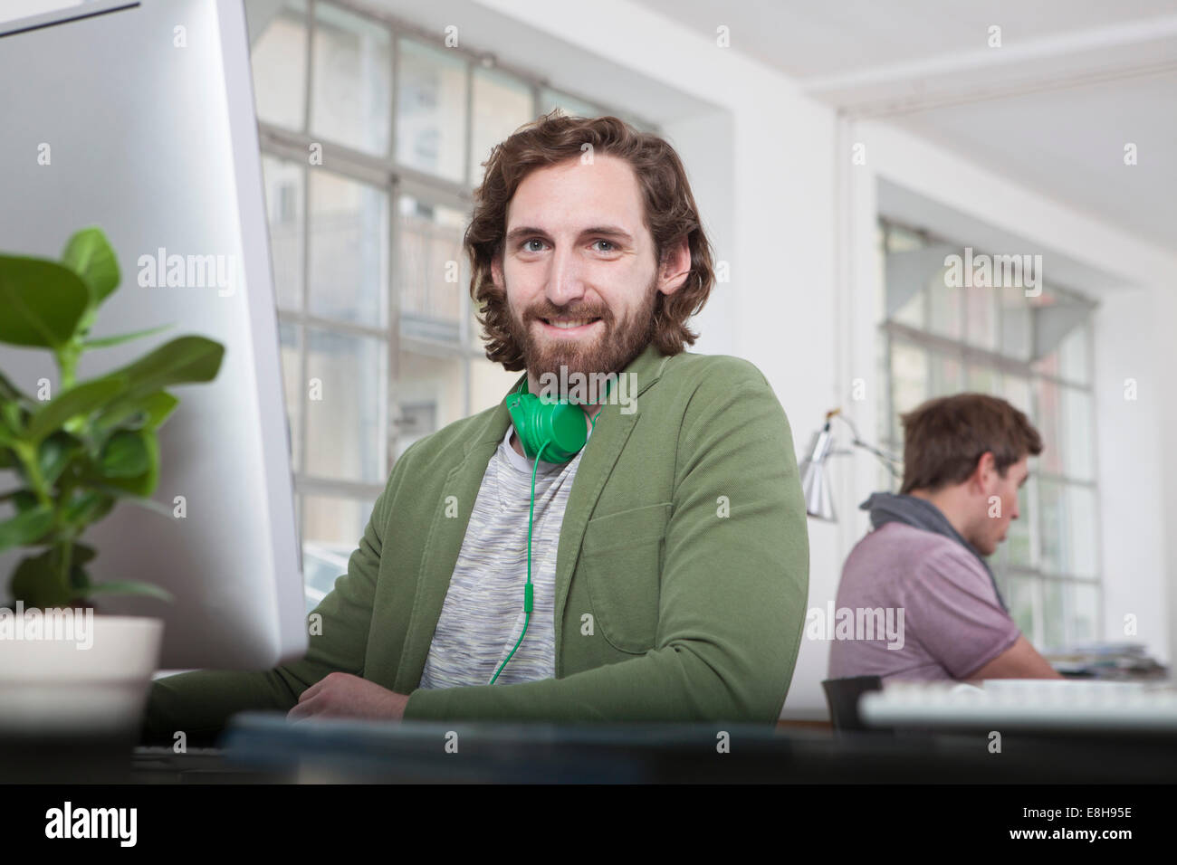 Porträt von lächelnden jungen Mann sitzt an seinem Schreibtisch in einem kreativen Büro Stockfoto