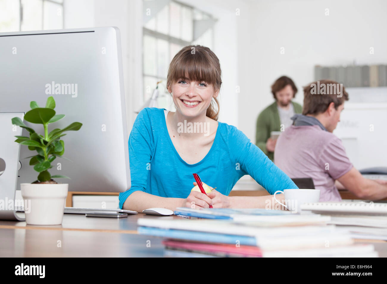 Porträt der lächelnde junge Frau sitzt an ihrem Schreibtisch in eine kreative Büro Stockfoto