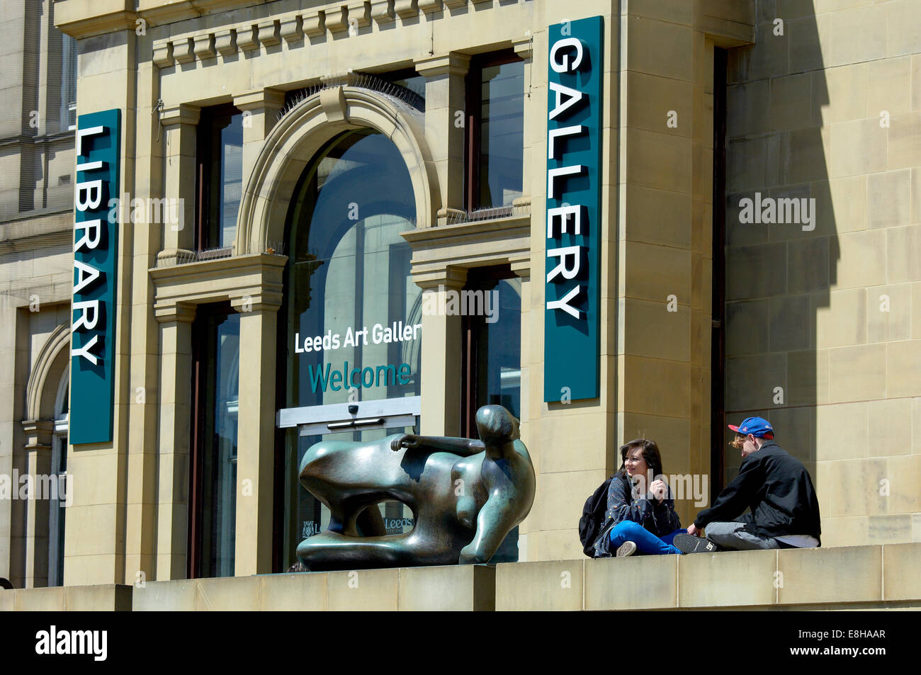 Leeds, UK. Junges paar entspannende neben Henry Moore Skulptur "Liegende Frau" außerhalb der Leeds Art Gallery, The Headrow. Stockfoto