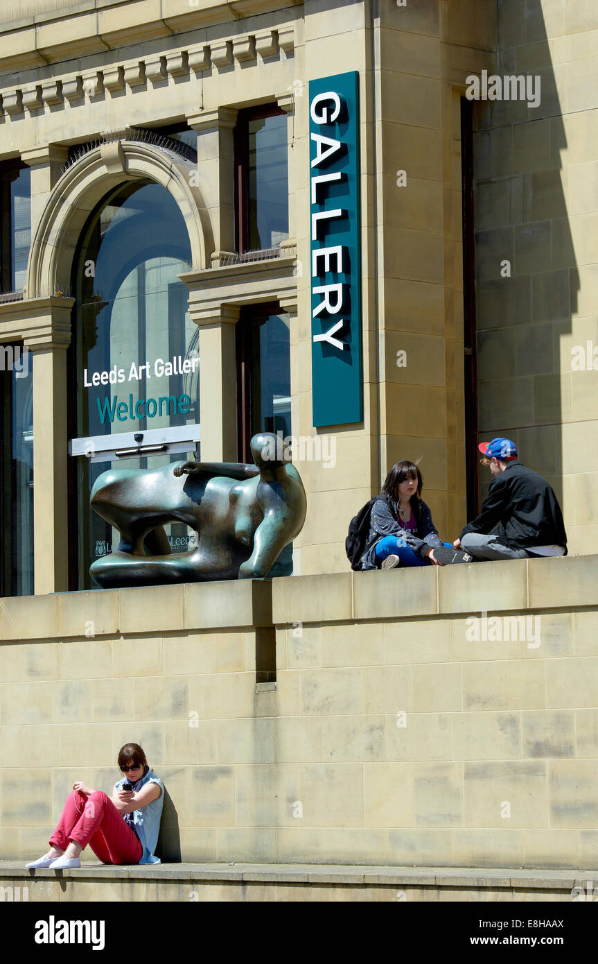 Leeds, UK. Menschen entspannen in der Sonne neben Henry Moore Skulptur "Liegende Frau" außerhalb der Leeds Art Gallery. Stockfoto