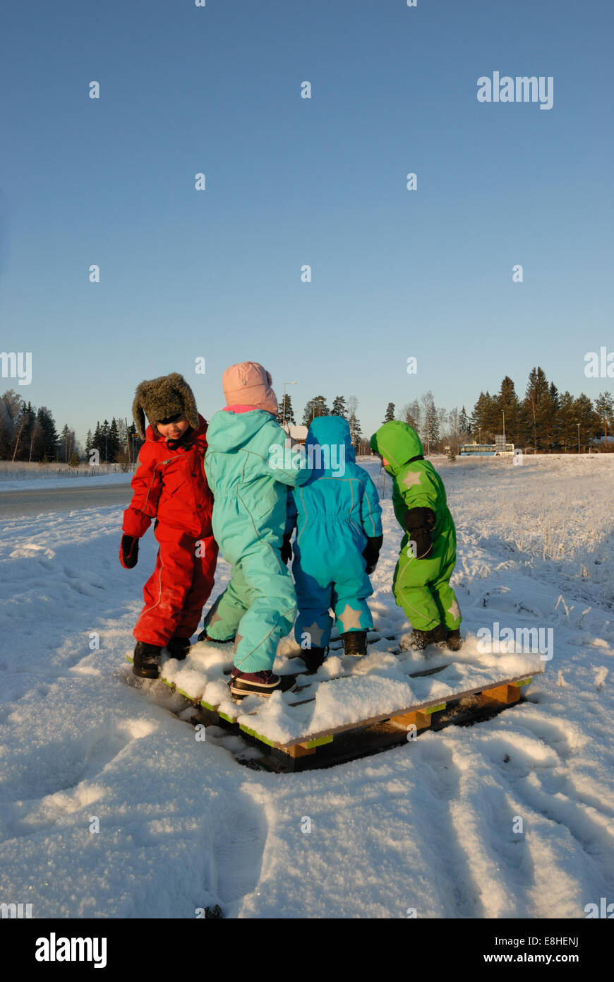 Kinder in bunten Winterkleidung spielen auf einem ausrangierten Holzpalette Stockfoto