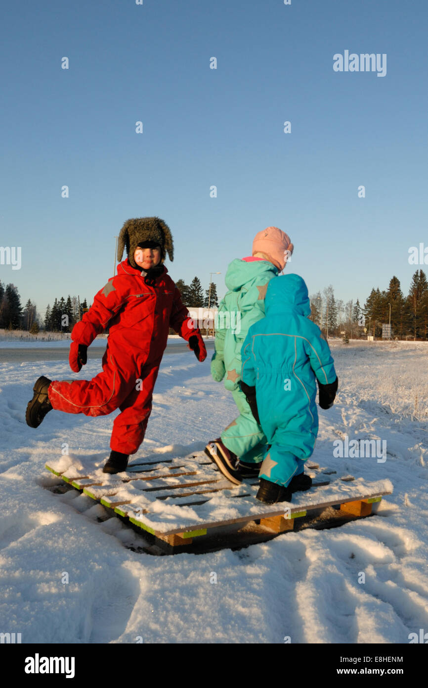 Kinder in bunten Winterkleidung tanzen auf einem ausrangierten Holzpalette Stockfoto
