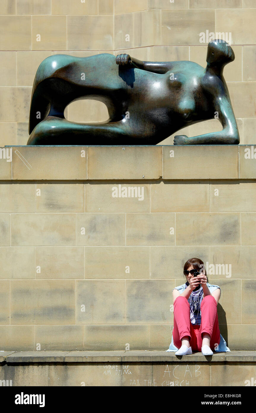 Leeds, UK. Junge Dame sitzt neben Henry Moore Skulptur "Liegende Frau" außerhalb der Leeds Kunst-Galerie & Bibliothek entspannen. Stockfoto