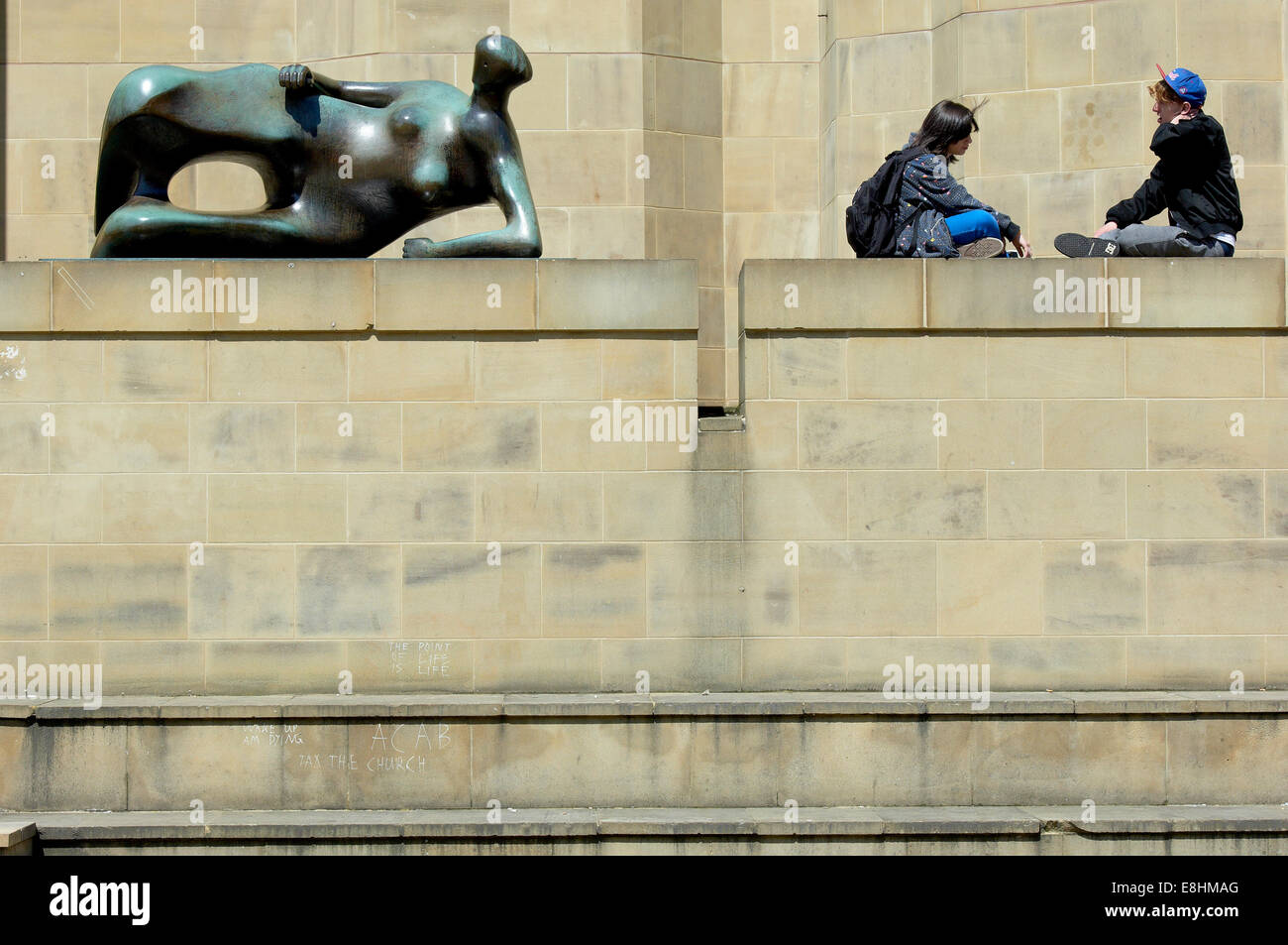 Leeds, UK. Junges paar entspannende neben Henry Moore Skulptur "Liegende Frau" außerhalb der Leeds Art Gallery, The Headrow. Stockfoto