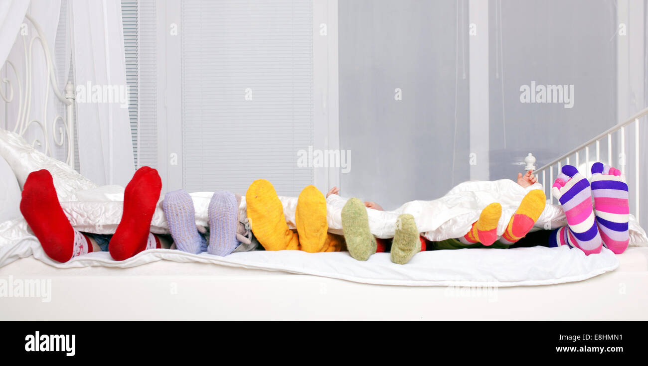 Glückliche Familien-Konzept. Füße aus Vater, Mutter und vier Kindern in bunten gestrickten Socken auf weißen Bett. Familie miteinander schlafen. Stockfoto