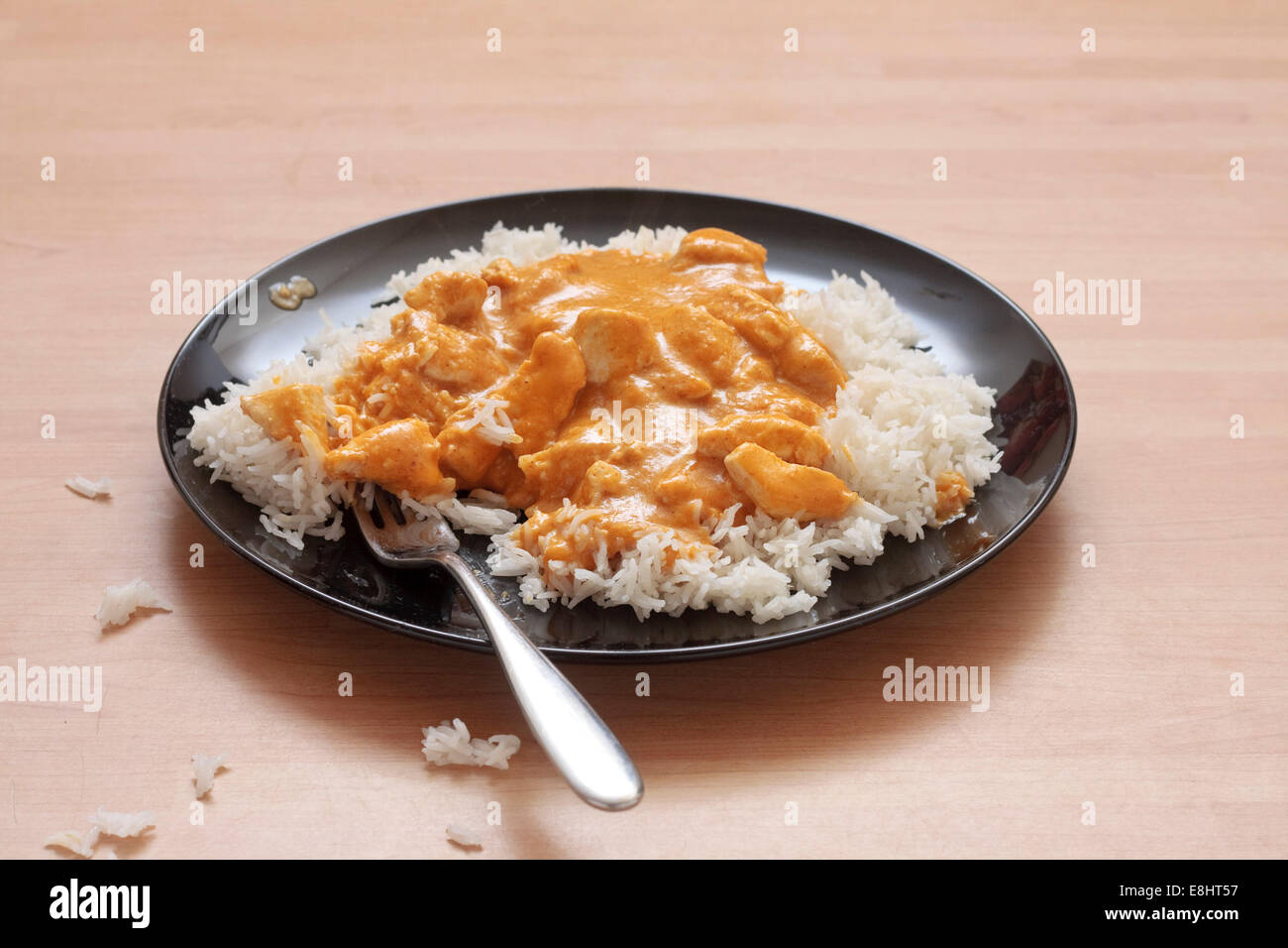 Ein Teller mit Chicken Korma und Reis auf einer schwarzen Platte mit abgelegten Reis um Platte auf Tisch Stockfoto