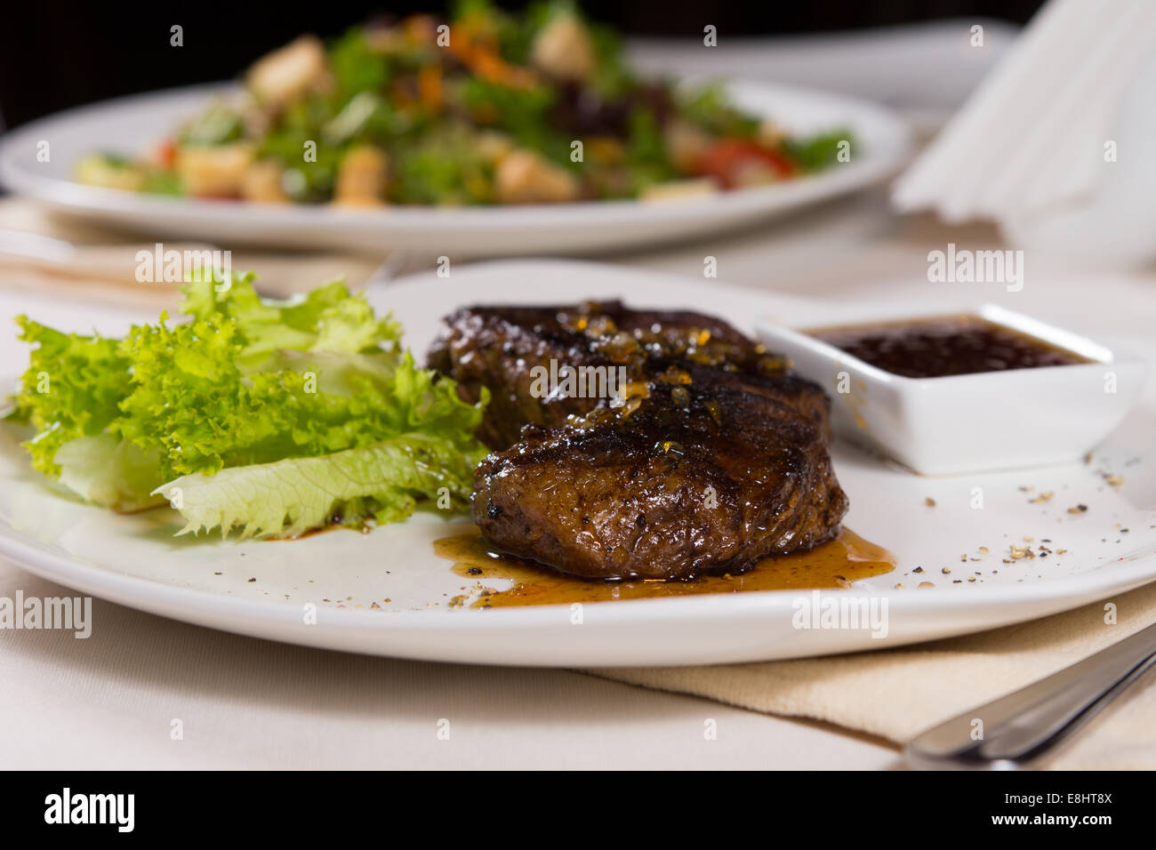 Saftiges Steak auf Teller mit Beilagen am Tisch im Restaurant mit anderen Gerichten Stockfoto