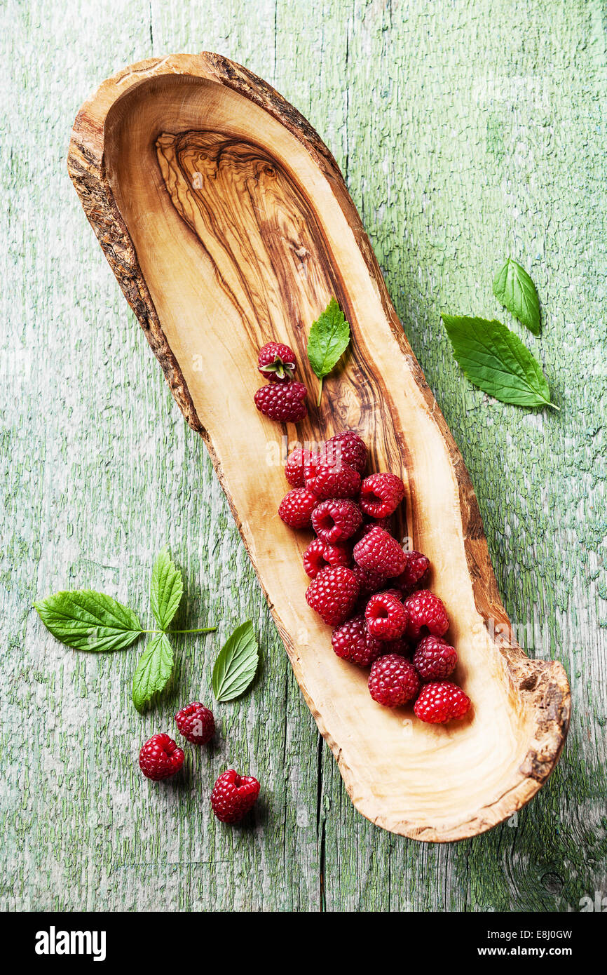 Himbeeren mit Blättern aus Olivenholz Schale auf grünem Hintergrund aus Holz Stockfoto