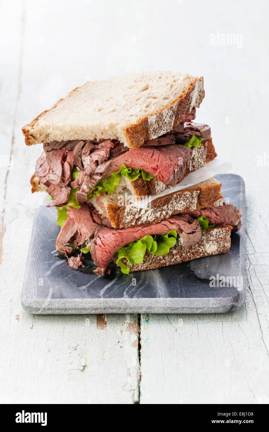 Roast Beef Sandwiches mit Salat auf Marmor Schneidebrett auf blauem Hintergrund Stockfoto