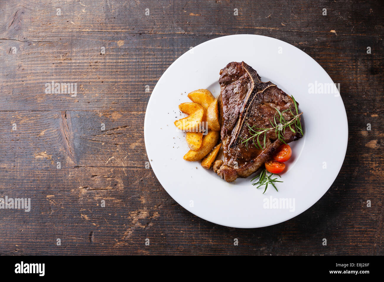 T-Bone Steak mit gebratene Kartoffelspalten auf weißen Teller auf hölzernen Hintergrund Stockfoto