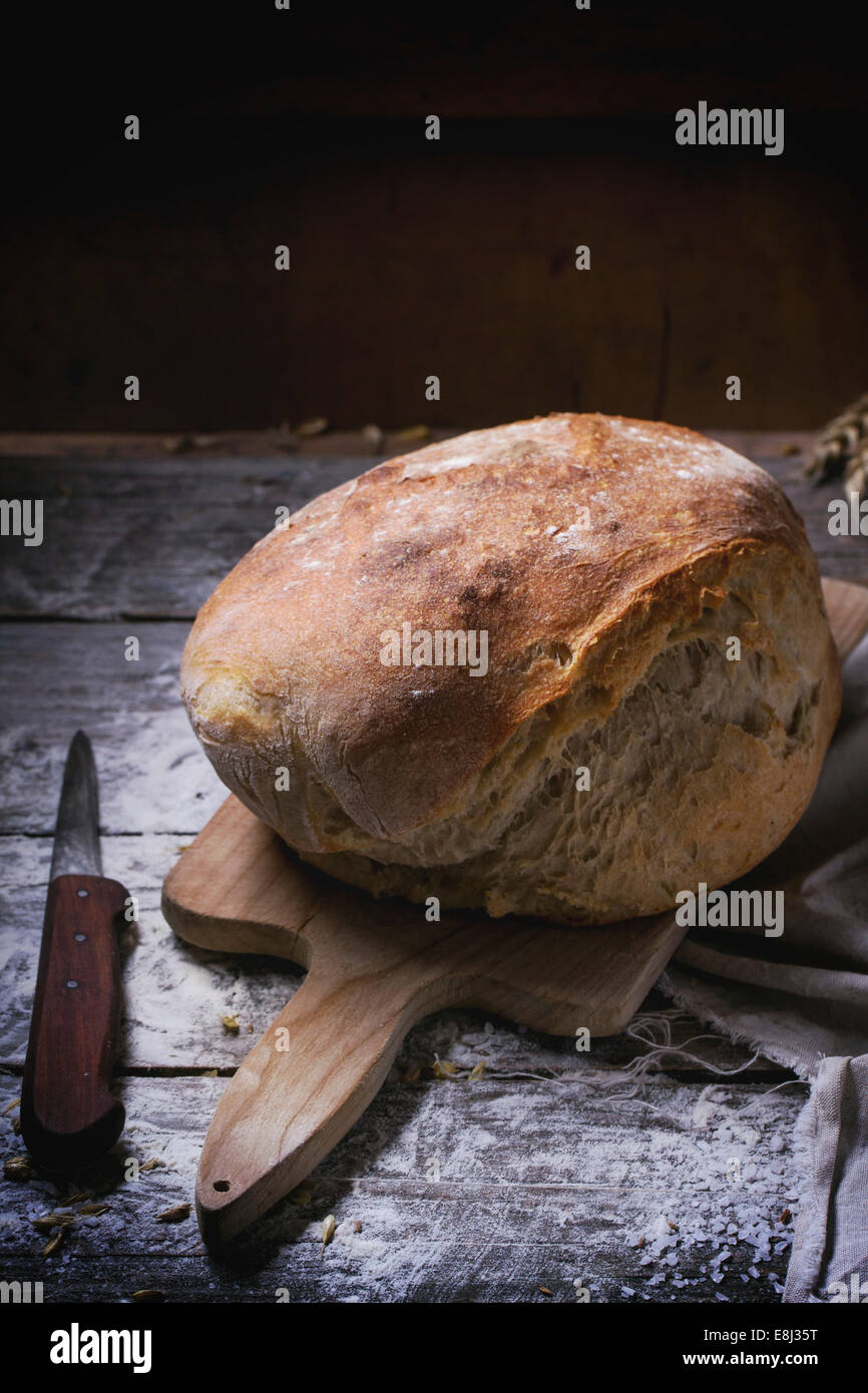 Frische hausgemachte Brot auf Holzbrett mit Vintage Messer diente über Holztisch mit Mehl Stockfoto