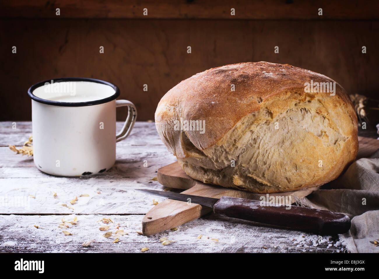Frische hausgemachte Brot auf Holzbrett mit Vintage Messer und Becher Milch mit Mehl über Holztisch serviert Stockfoto