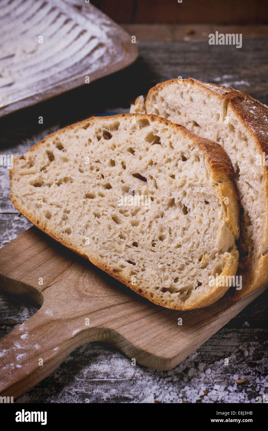 In Scheiben selbstgebackenes Brot auf Holzbrett serviert auf Holztisch mit Mehl. Serien ansehen Stockfoto