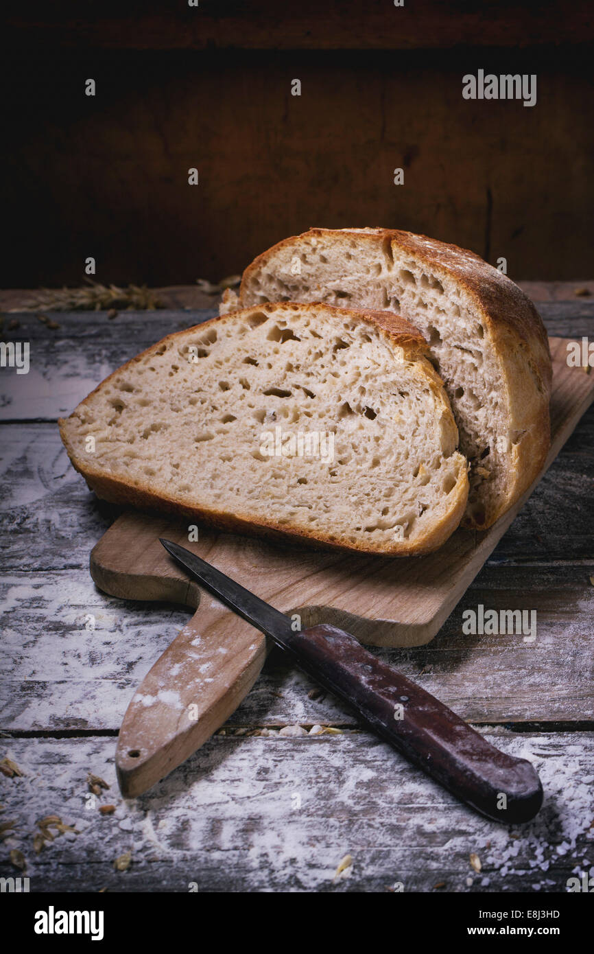 In Scheiben selbstgebackenes Brot auf Holzbrett serviert auf Holztisch mit Mehl Stockfoto