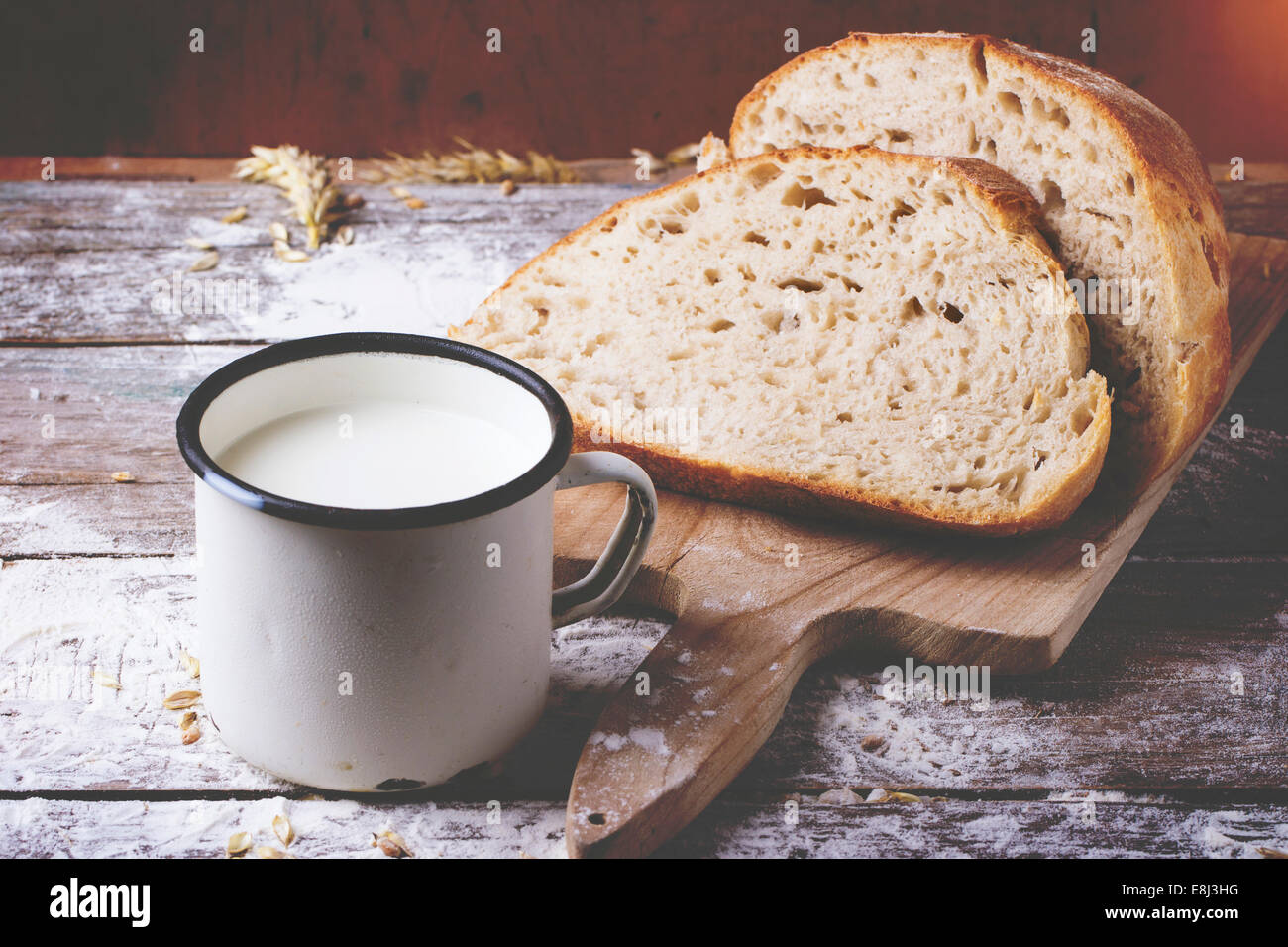 In Scheiben selbstgebackenes Brot auf Holzbrett und Becher Milch mit Mehl über Holztisch serviert. Retro-Filter-Effekt. Stockfoto