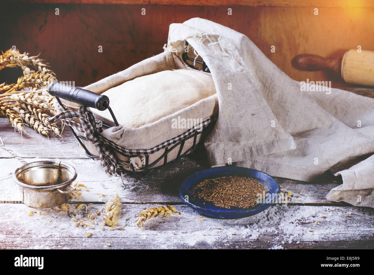 Brot backen. Teig in proofing Korb auf Holztisch mit Mehl, Kümmel und Weizen Ohren. In Retro-Filter-Effekt Stockfoto