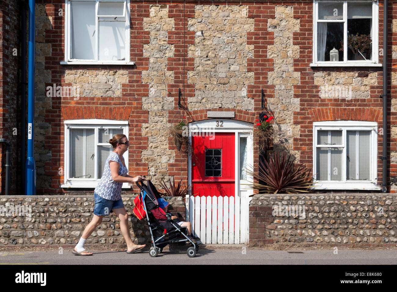 Frau mit Kind im Buggy vorbei an Haus mit roten Tür, Selsey, West Sussex Stockfoto