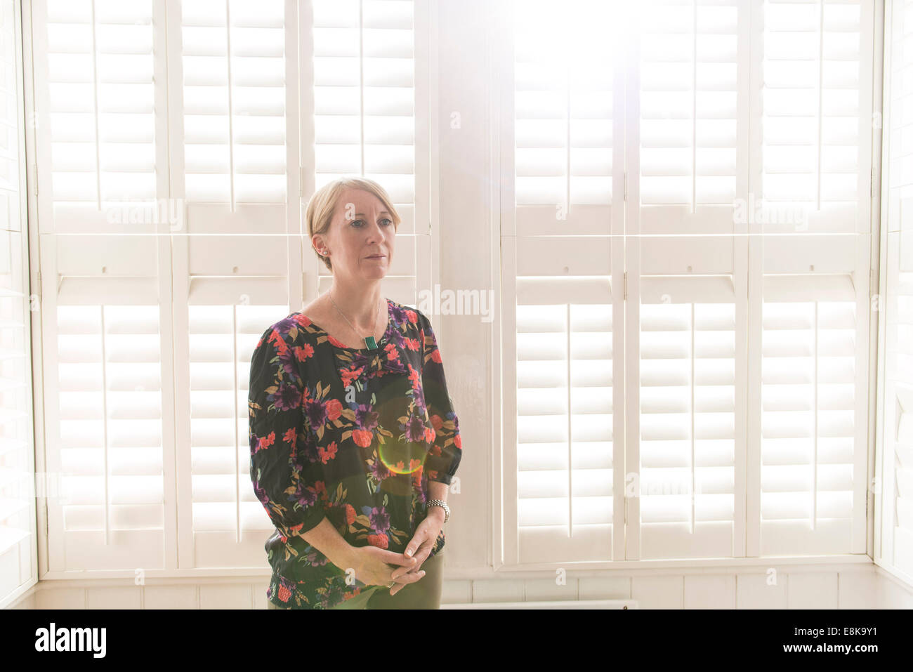 Eine Business-Frau / Mutter mit kurzen Haaren steht durch Jalousien in interessanten Licht Stockfoto