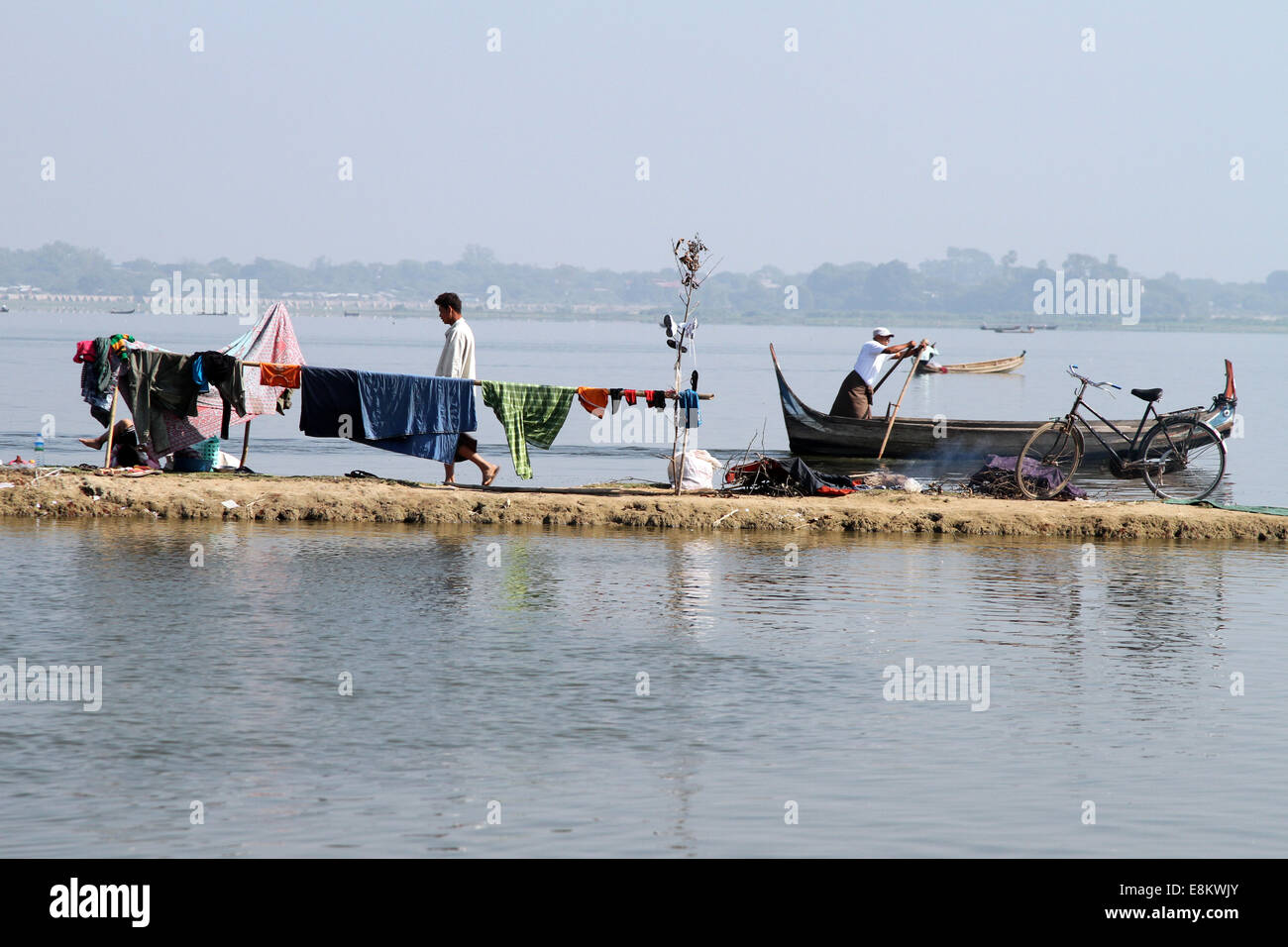 Ein Mann geht vorbei an einem Ruderboot und trocknende Wäsche am Taungthaman-See, Amarapura, Birma (Myanmar) Stockfoto