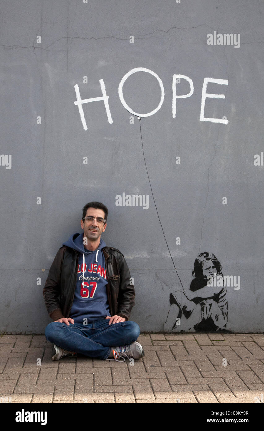 London, UK. 10. Oktober 2014. 10. Oktober 2014 - Mann sitzt neben angeblichen Banksy Wandbild 'Hope' an Wand in Northcote Road - London-UK-Credit: M.Sobreira/Alamy Live News Stockfoto