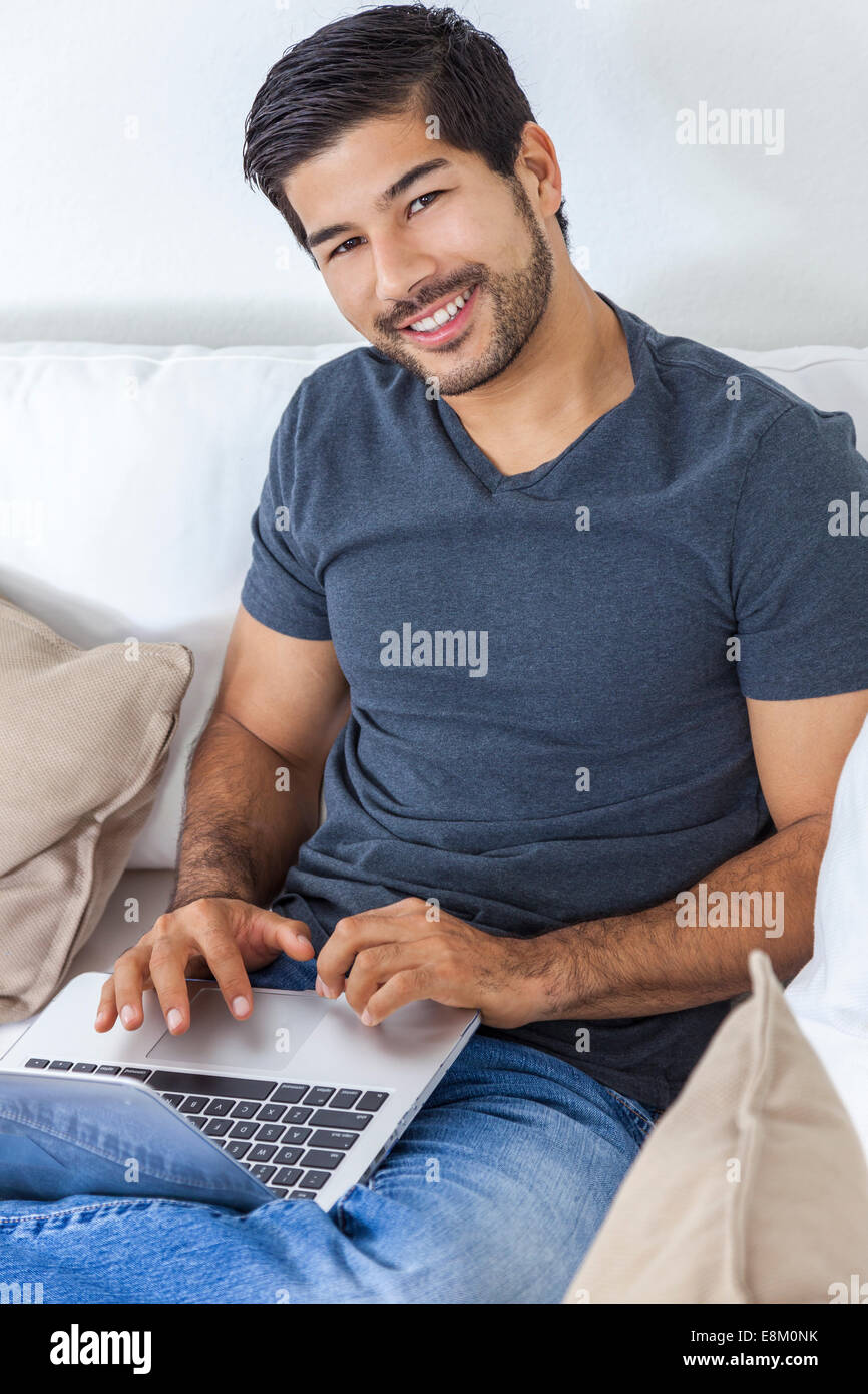 Porträt der schönen lächelnden jungen asiatischen Mann mit einem Bart mit Laptop-Computer zu Hause Stockfoto