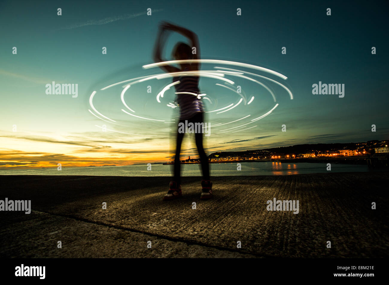 Eine Frau in Silhouette Hula hooping mit einer beleuchteten Hula-Hoop in der Abenddämmerung Dämmerung - Langzeitbelichtung Lichtspuren Kreise Aberystwy Stockfoto