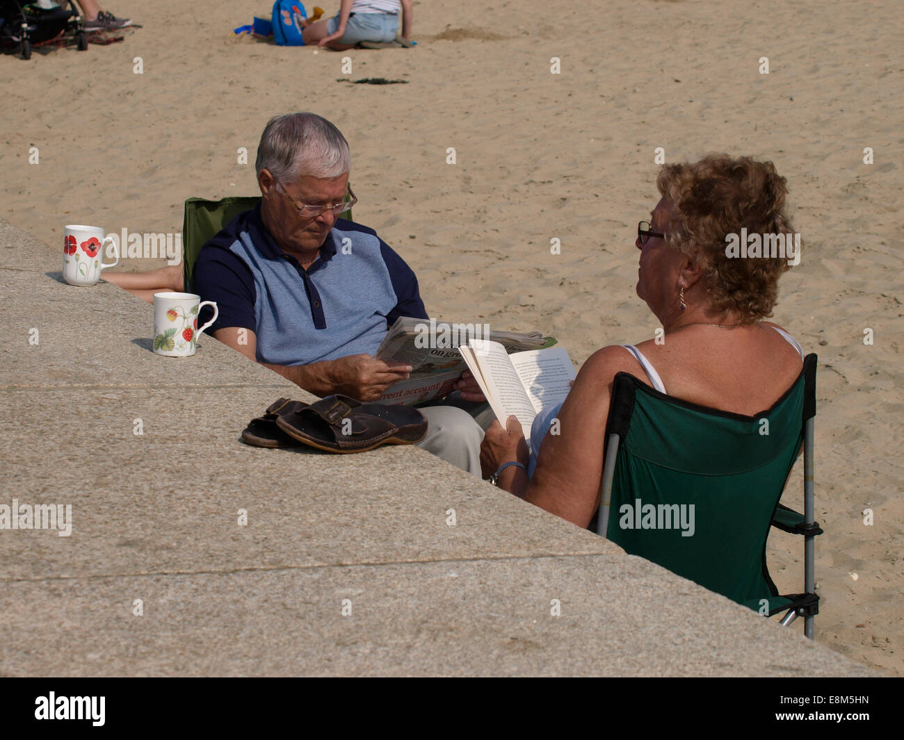 mittleren gealterten paar saß am Strand lesen, Lyme Regis, Dorset, Großbritannien Stockfoto