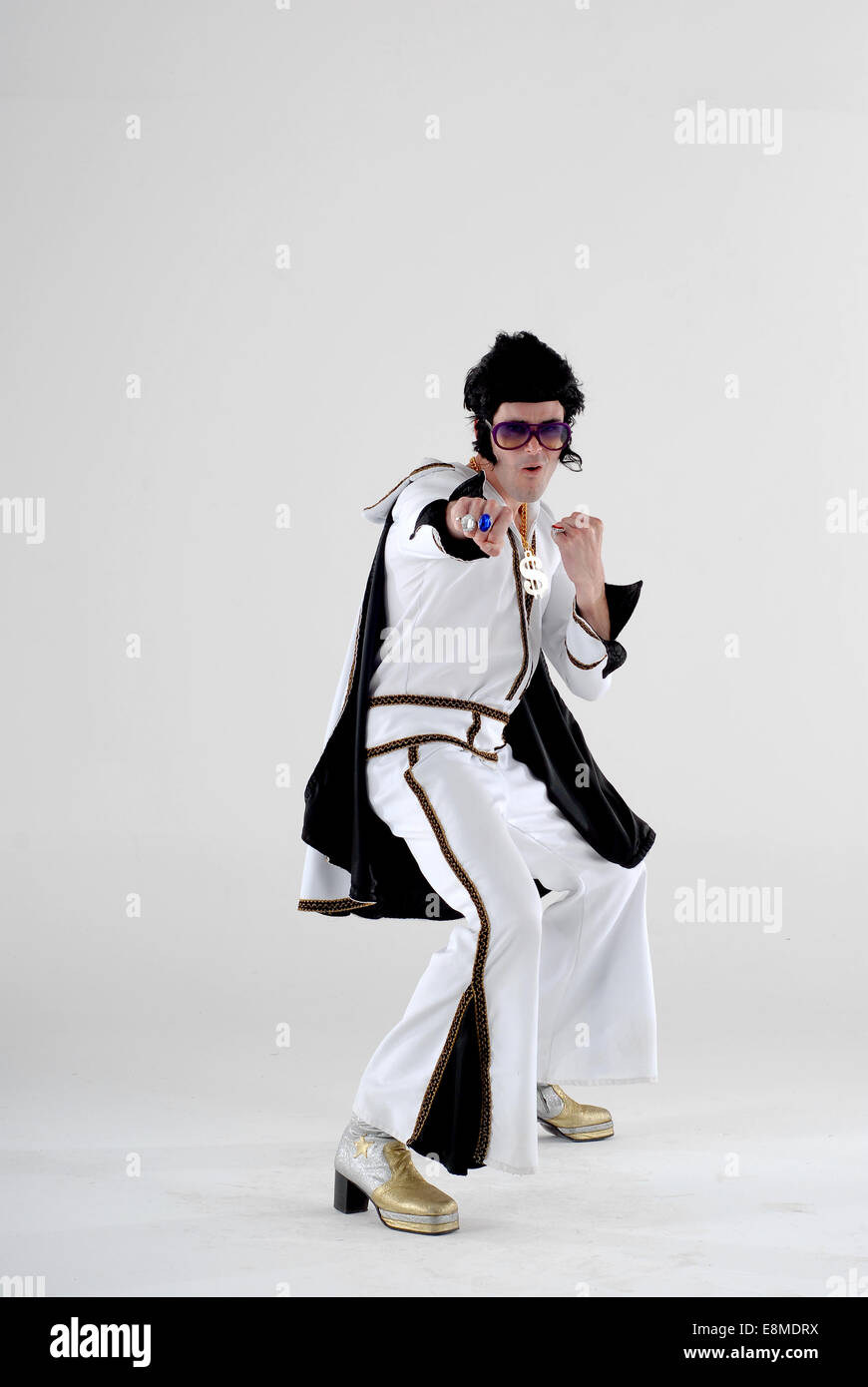 Mann gekleidet in Kostüm, Komödie Kostüm als Elvis, in voller Höhe bei der 1970er Jahre Sprunganzug mit Fackeln, Perücke, Sonnenbrille und Plattform Stiefel Stockfoto