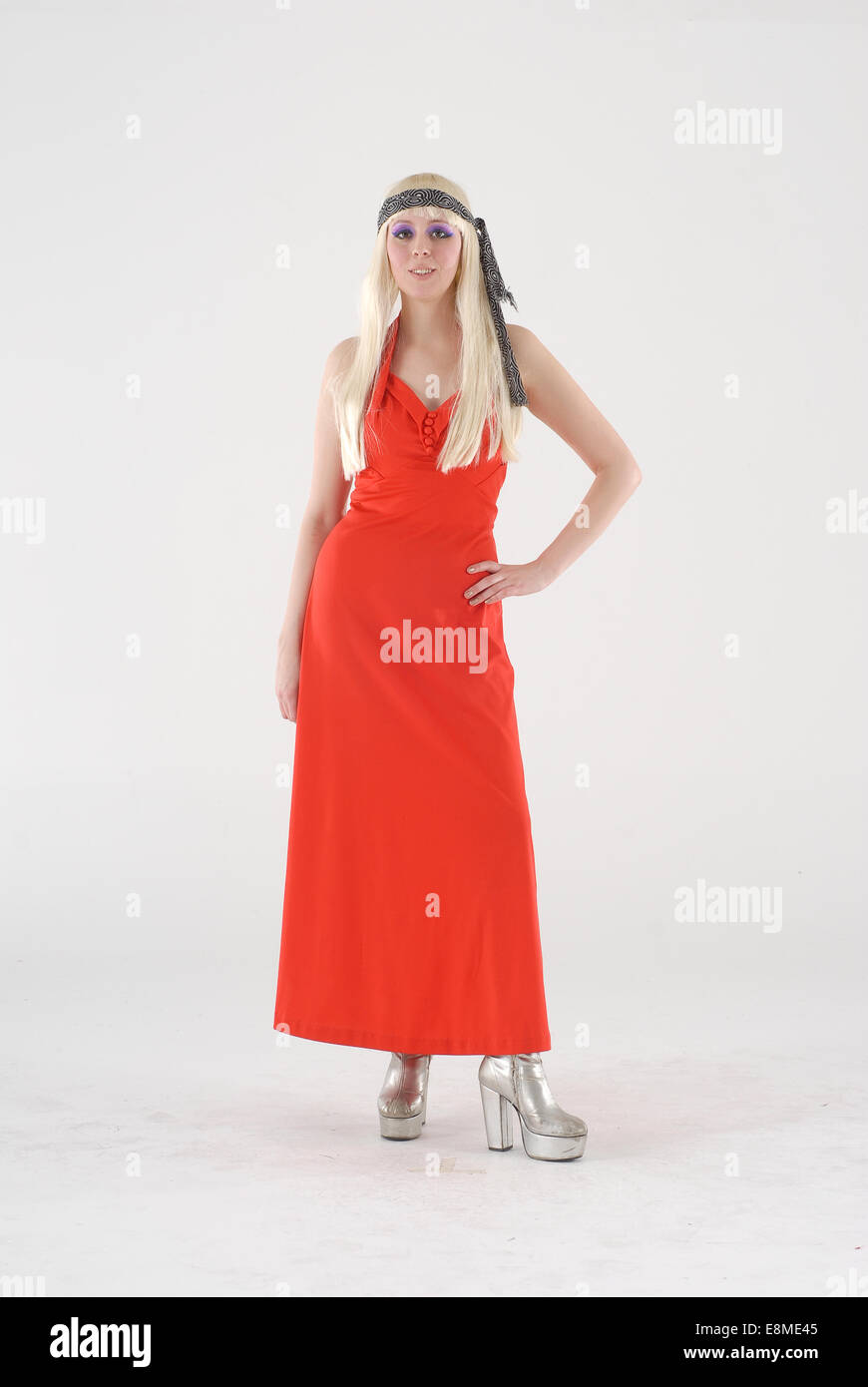 Mädchen in Komödie Kostüm gekleidet in ein 1970er Jahre / 1960er Jahre Hippie / Blumenkind Outfit & rotes Kleid, Perücke & Stiefel Silber Stockfoto