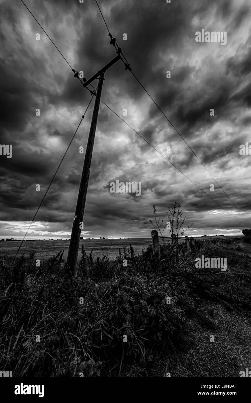 Silhouette der einen Telegrafenmast in der Abenddämmerung mit wütenden dunkle Wolken am Himmel in schwarz / weiß Stockfoto
