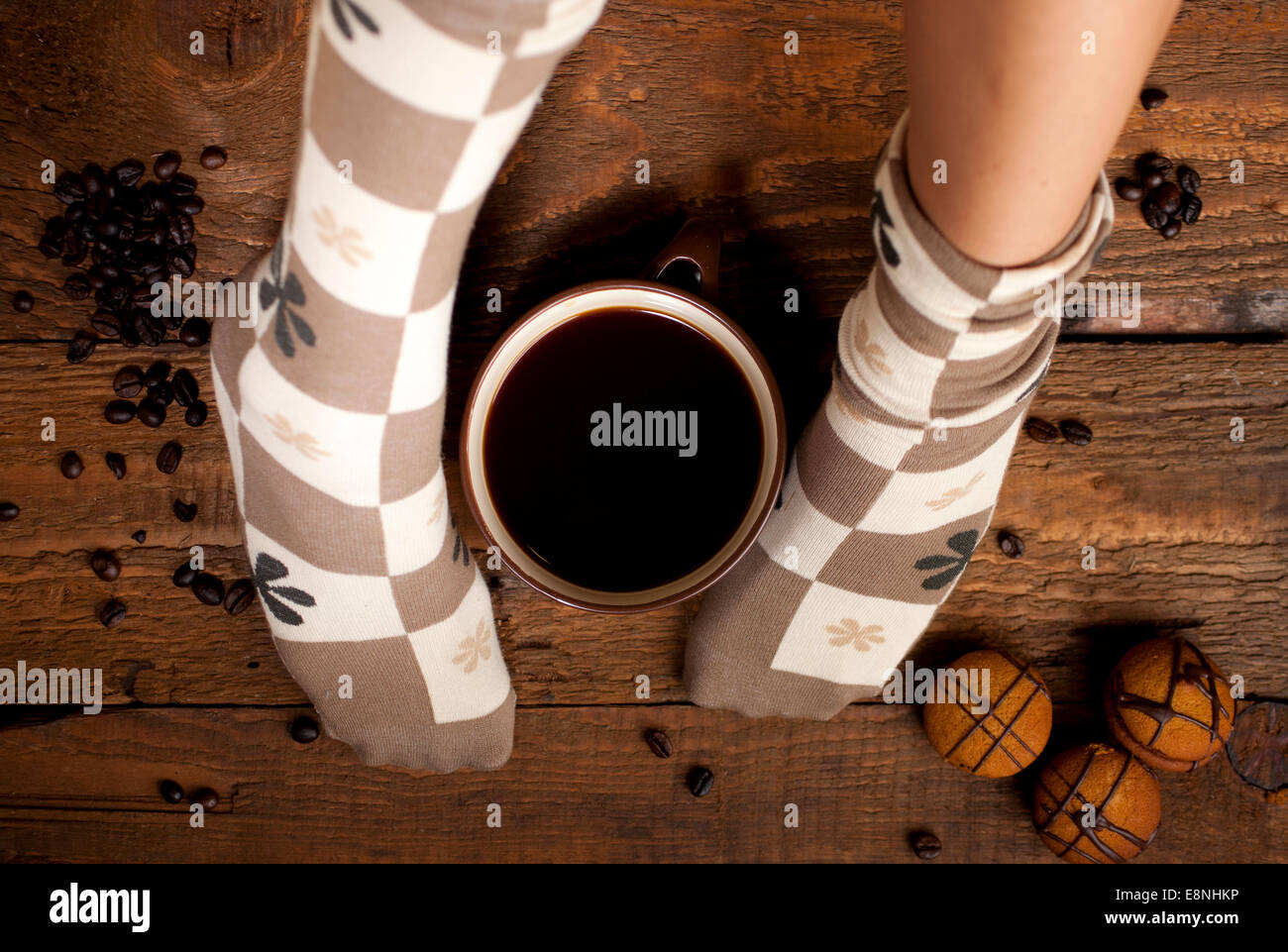 Eine Tasse Kaffee oder heiße Schokolade und weibliche Füße mit süßen braunen Socken auf einem hölzernen Hintergrund. Stockfoto