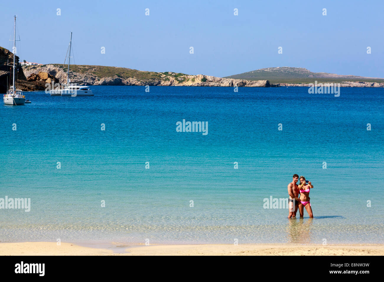 Mann und Frau im Urlaub mit dem "Selfie" fotografieren stehen im Meer in Arenal d ' en Castell, Menorca, Spanien Stockfoto