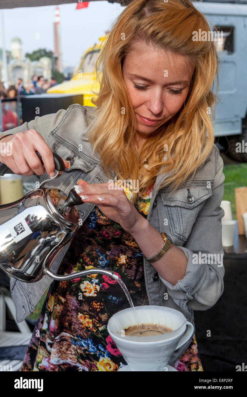 Eine Frau gießt Kaffee, gießt ein heißes Getränk in eine Tasse, Prager Street Food Festival Barista Woman Jeans Jacke Stil bereitet heißes Getränk zu Stockfoto