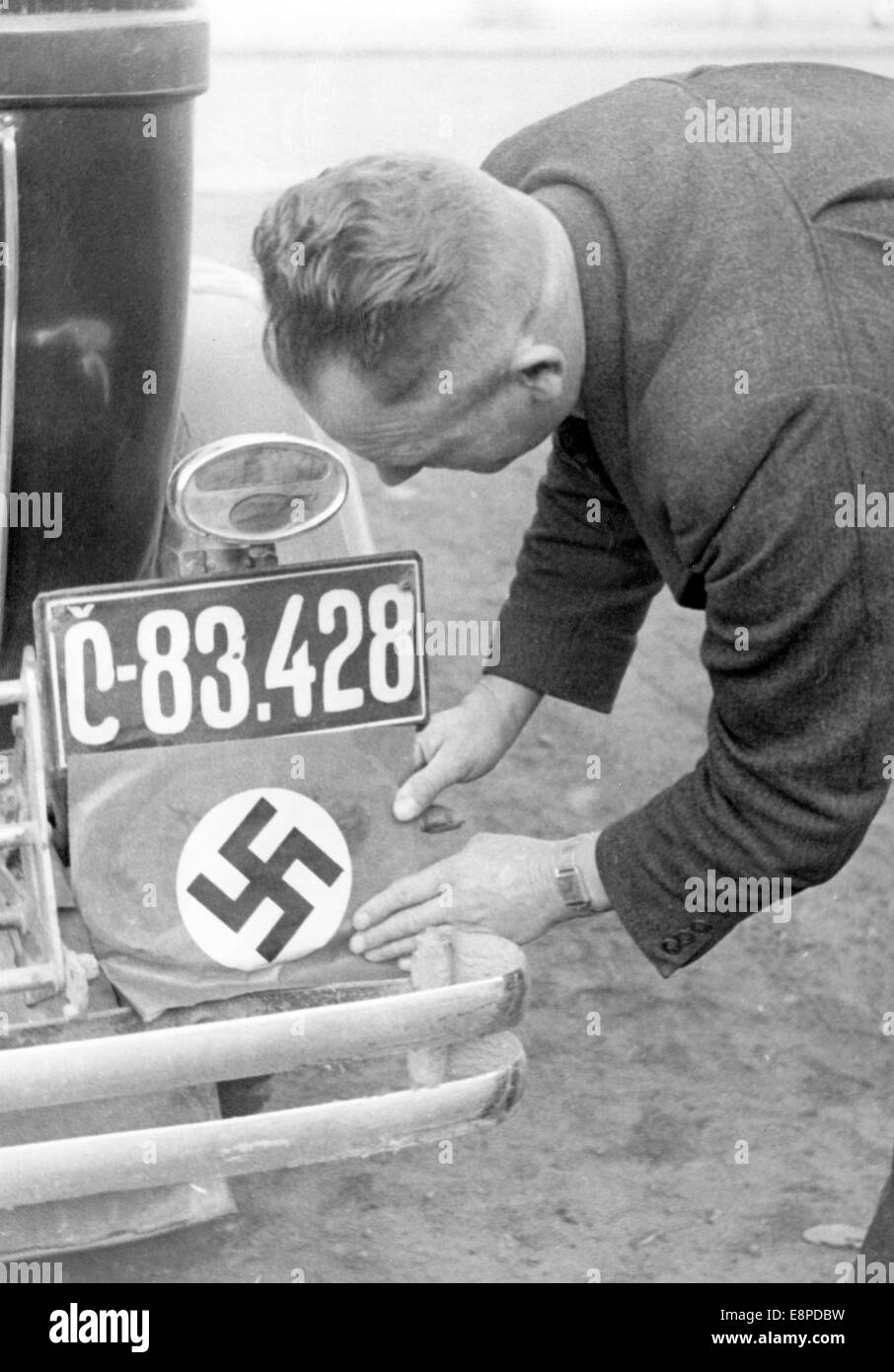 Das Nazi-Propagandafild zeigt einen Mann aus Sudetenland, der sein tschechoslowakisches Nummernschild im Vorfeld des Münchner Abkommens im September 1938 mit einem Hakenkreuz bedeckt. Der Originaltext eines Nazi-Nachrichtenberichts auf der Rückseite des Bildes lautet: "Sie wollen nichts mehr mit den Hussiten zu tun haben. Ein Sudetenland-Deutscher deckt den gehassten CS-Ländercode mit einem Hakenkreuz auf seinem Nummernschild ab. Fotoarchiv für Zeitgeschichtee - KEIN KABELDIENST Stockfoto