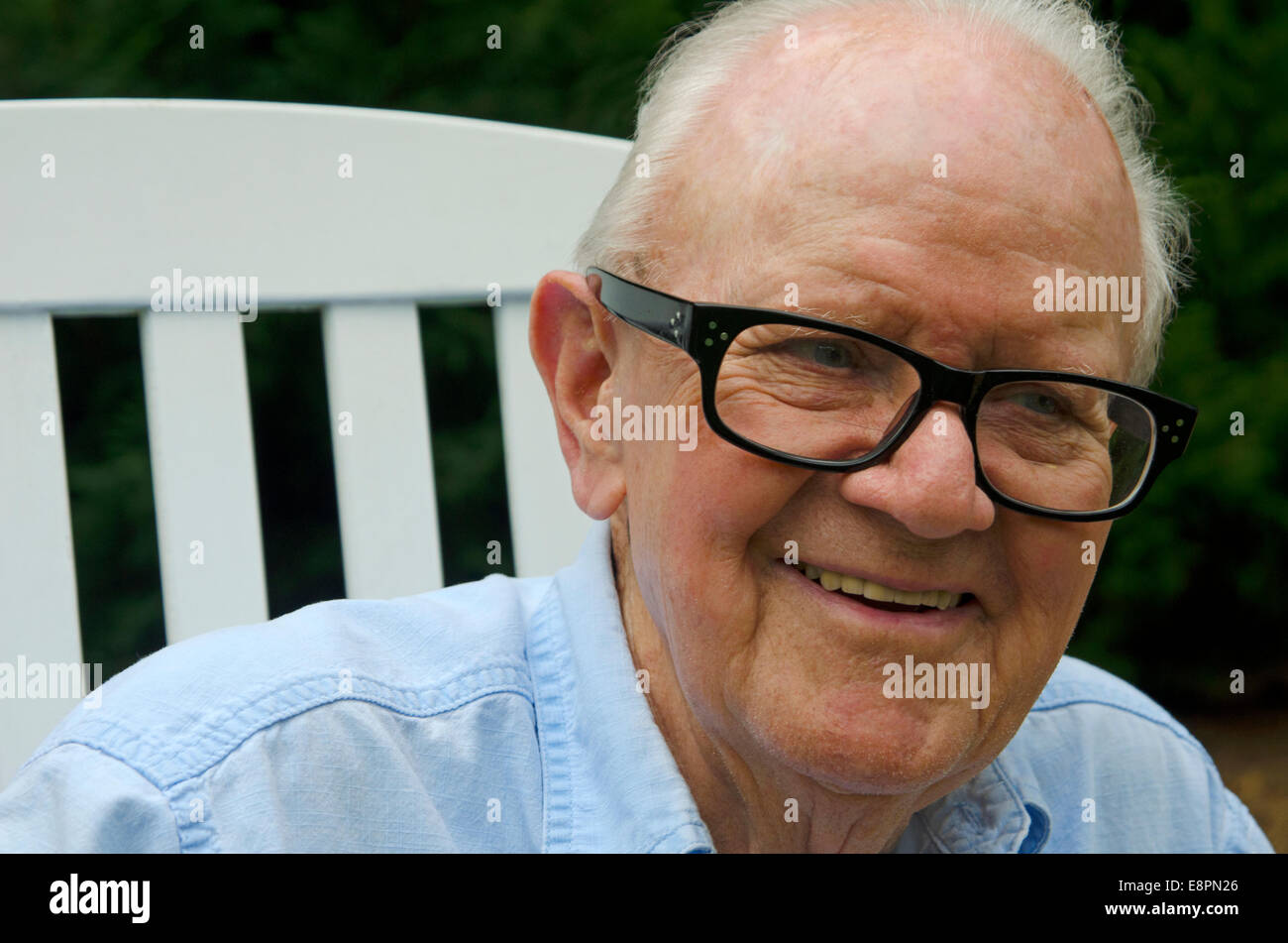 Porträt von ein älterer Herr in einem weißen Schaukelstuhl hautnah. Thema ist Lächeln auf den Lippen und auf der Suche von der Kamera entfernt. Stockfoto