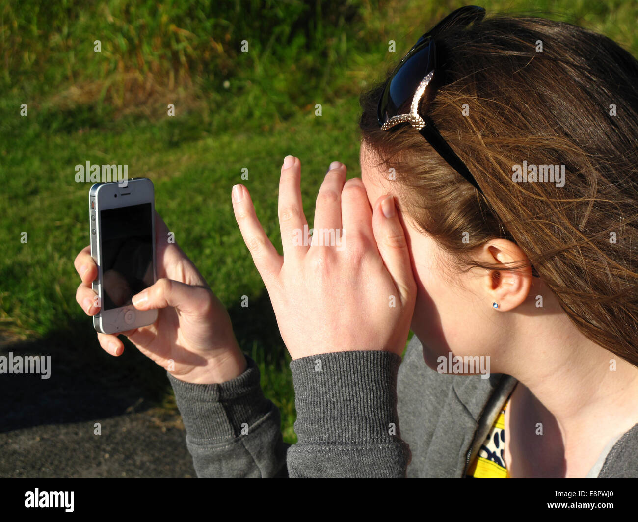 Junge Teenager-Mädchen mit iPhone bei starker Sonneneinstrahlung Stockfoto