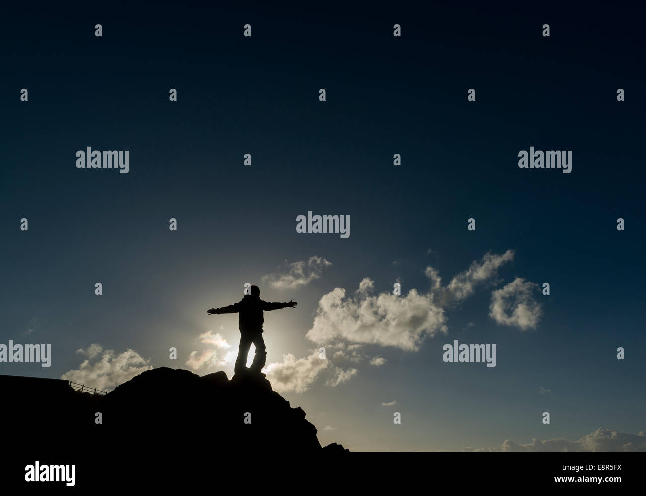 Ein Junge genießt die Freiheit, wie er auf schroffen Felsen Silhouette gegen die Sonne und Himmel an der Küste von Nord-Devon, UK spielt Stockfoto