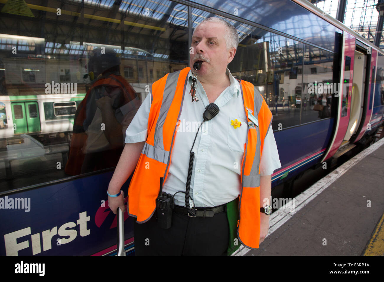 Ein Signalmann an einem Bahnhof bereitet sich darauf vor, Pfeifen zu blasen, um den Fahrer zu benachrichtigen, sich zu ziehen. Brighton Bahnhof Stockfoto