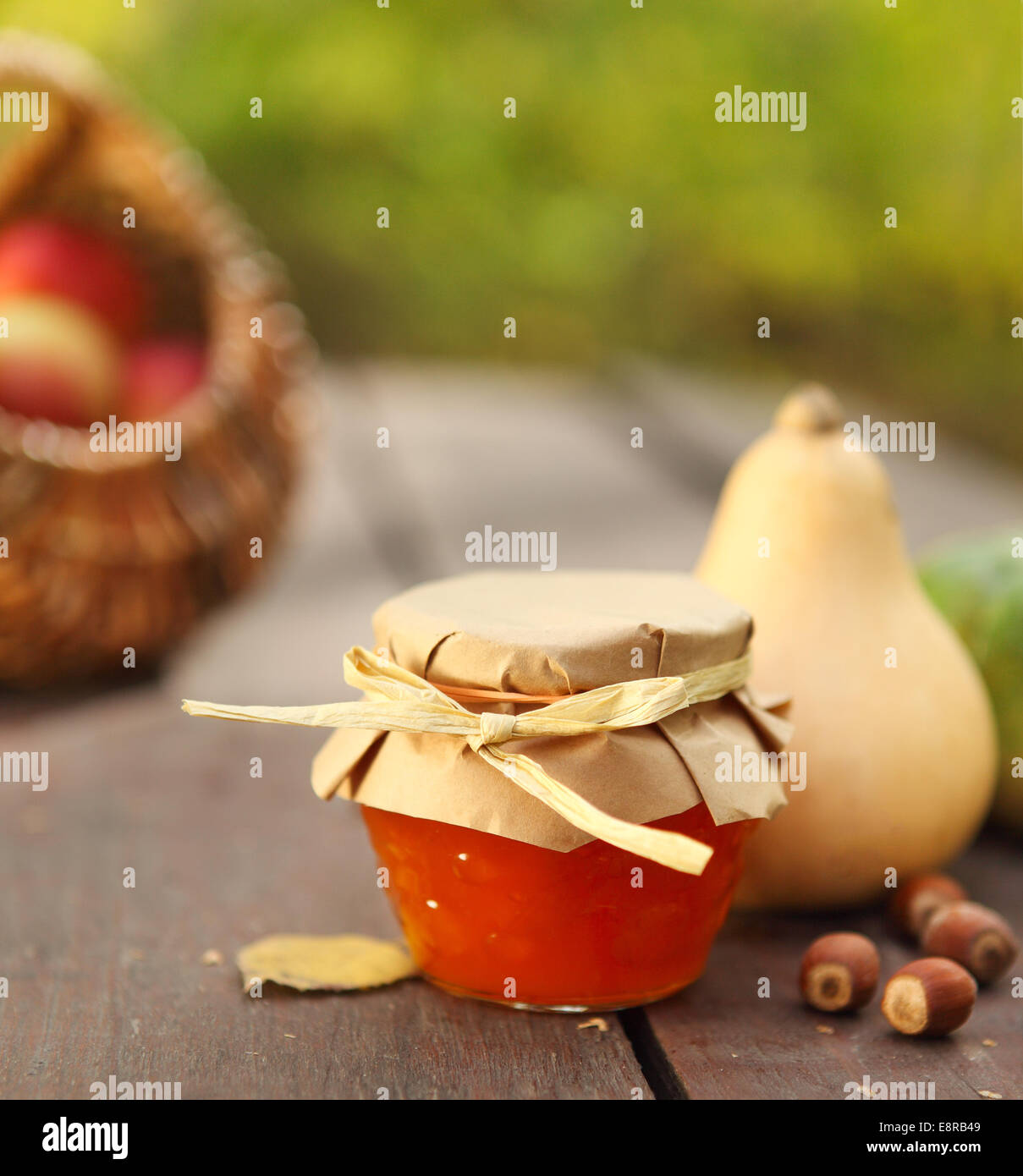 Kürbisse, Marmelade, Nüssen und Korb mit Äpfeln auf Gartentisch Stockfoto