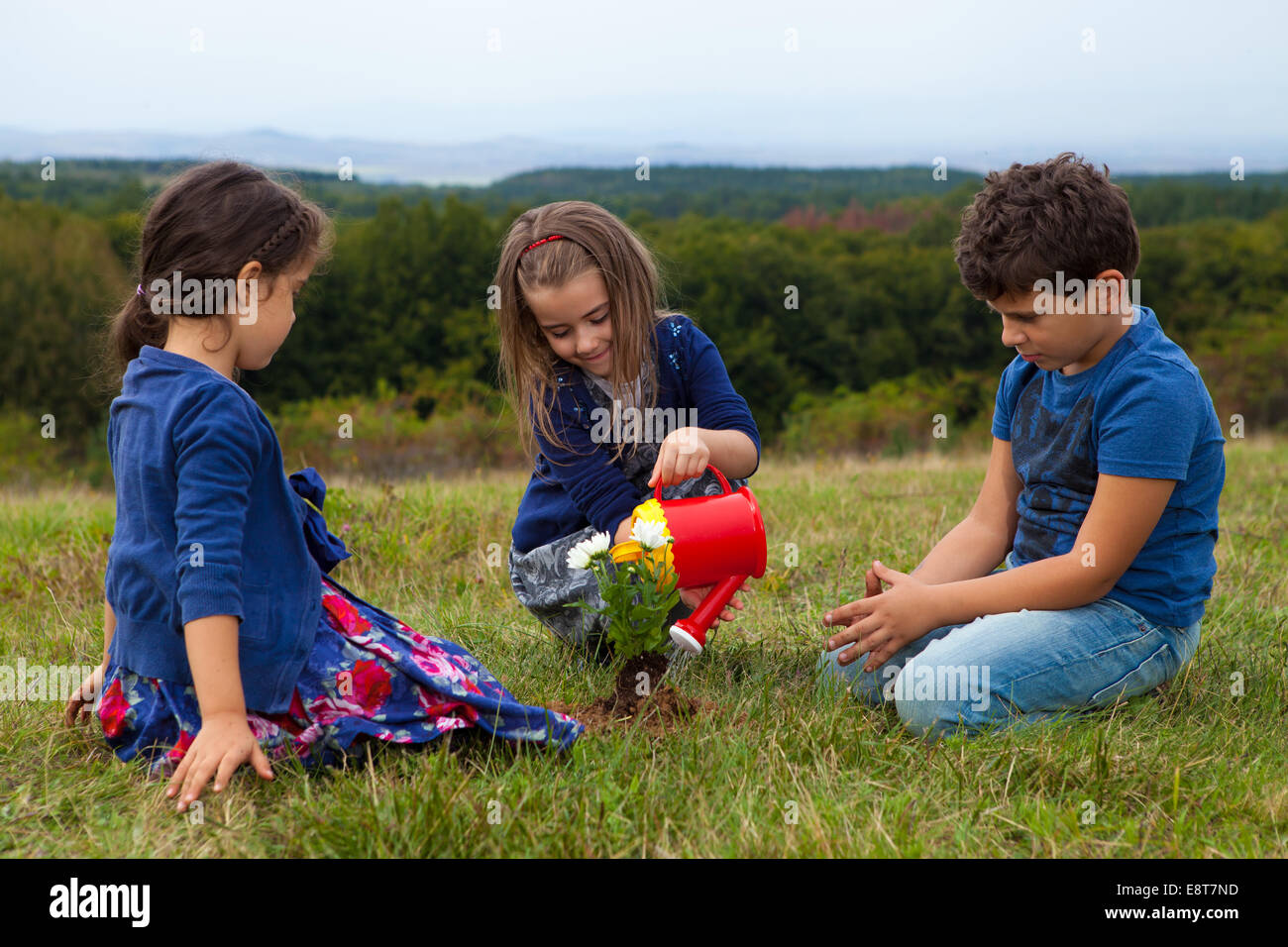 Kinder im Garten und Bewässerung von Pflanzen mit einer Spielzeug-Kunststoff-Gießkanne Stockfoto