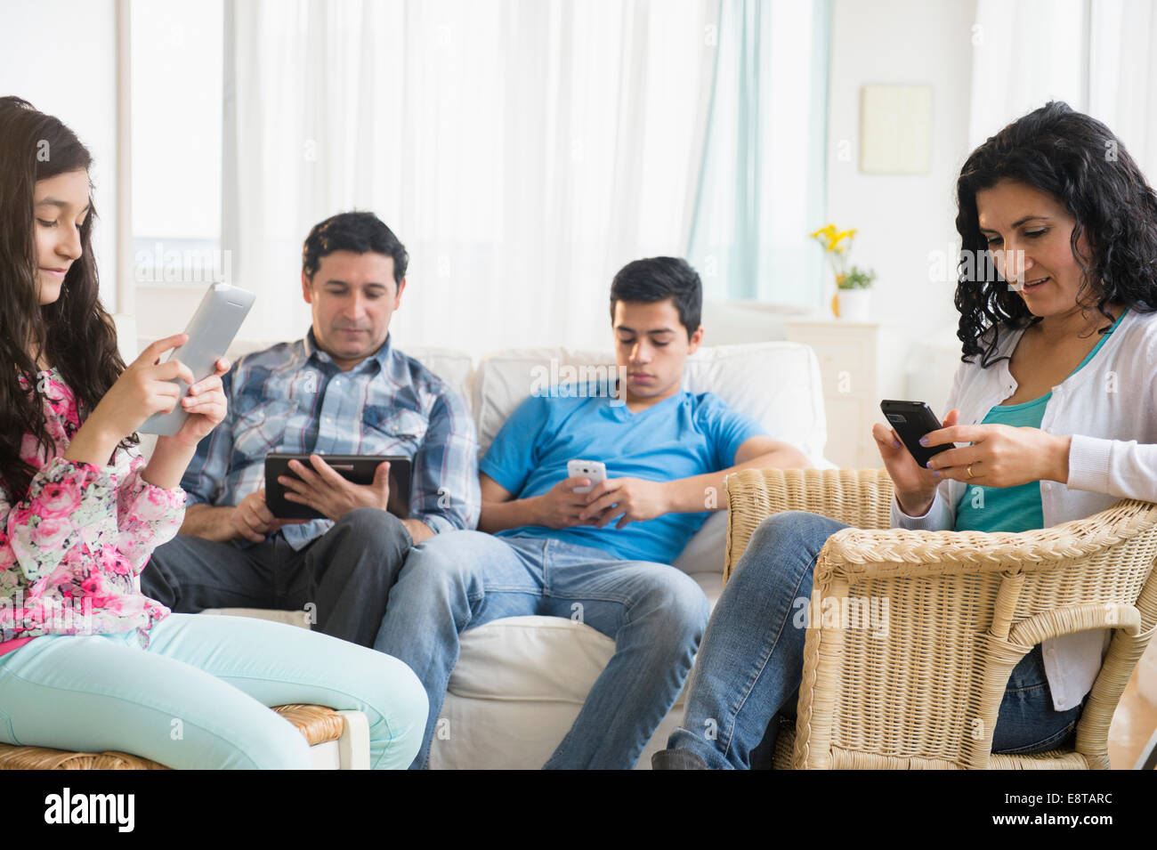Spanische Familie mit Handys und digitalen Tablets im Wohnzimmer Stockfoto